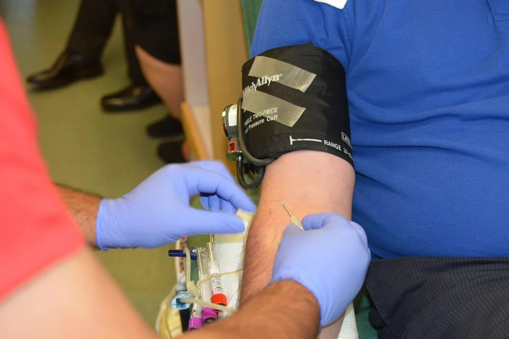A nurse in blue gloves preparing a donor’s arm, with a blood pressure cuff on